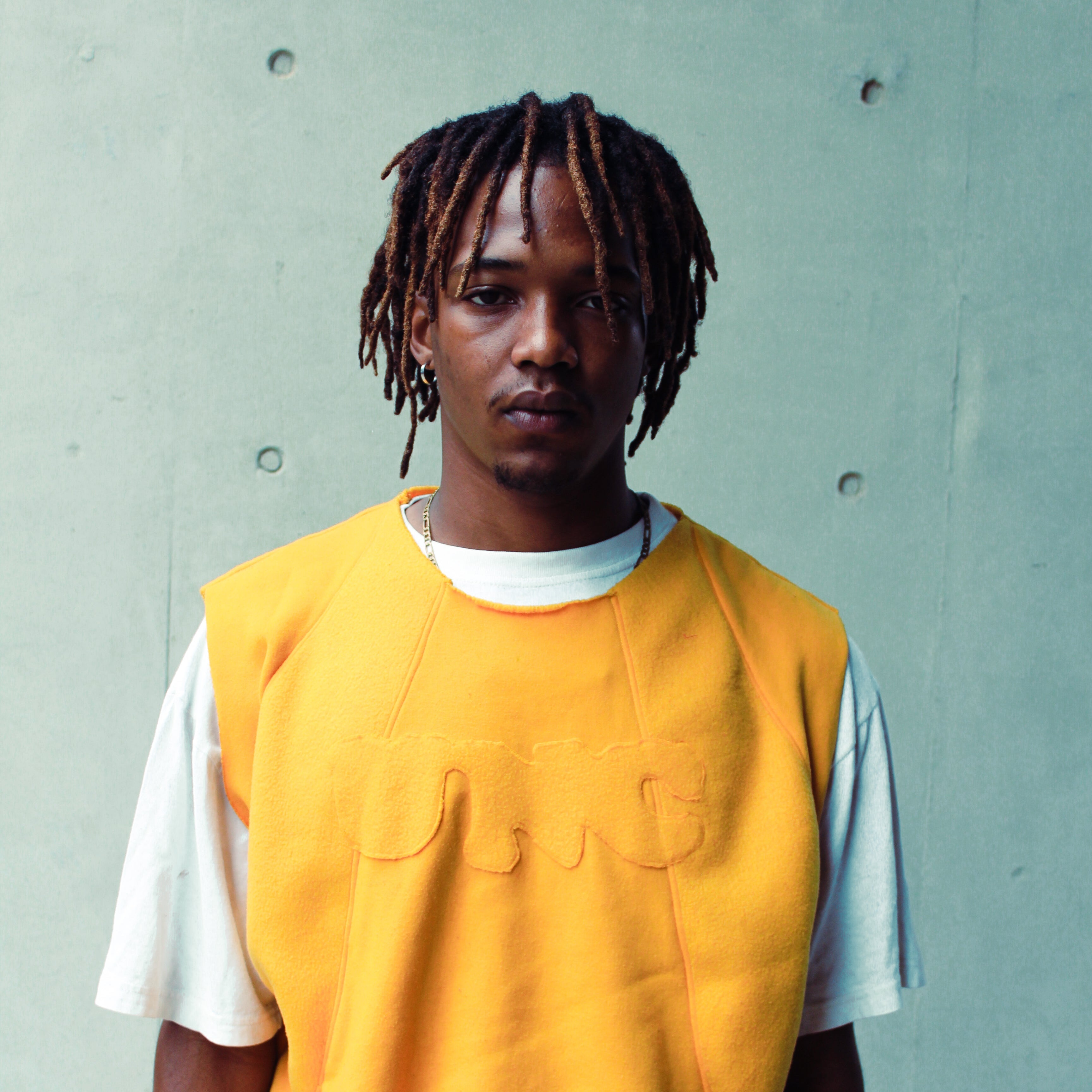 Person wearing a yellow vest over a white shirt against a gray concrete wall