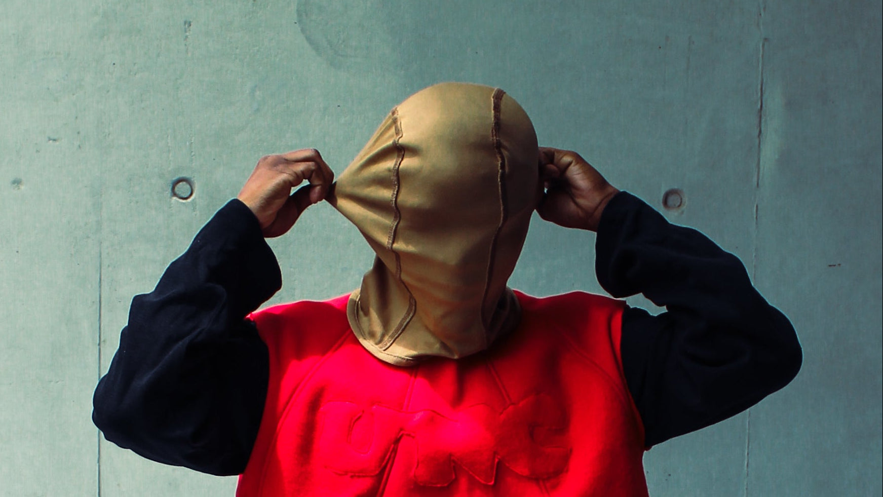 Person wearing a red sleeveless top and black shorts standing against a concrete wall.
